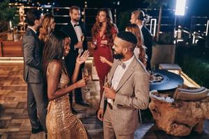 Group of beautiful young people in formalwear communicating and smiling while spending time on luxury party photo