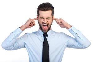 Too loud sound  Frustrated young man in shirt and tie covering ears with fingers and keeping eyes closed while standing against white background photo