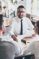 Congratulations Two men sitting at the desk and shaking hands while young woman looking at them photo