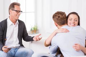 Together again. Happy young couple hugging while sitting together with psychiatrist photo