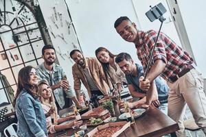 grupo de jóvenes modernos tomándose selfie usando un teléfono inteligente mientras cenan foto