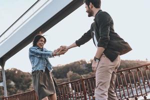 They belong together. Beautiful young couple holding hands and spinning while standing on the bridge outdoors photo