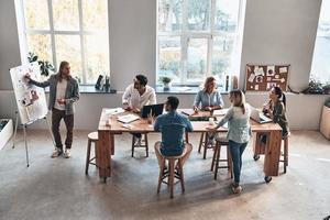 cooperación en acción. vista superior del joven moderno que realiza una presentación de negocios mientras está de pie en la sala de juntas foto