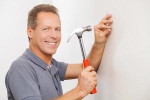 Cheerful handyman. Cheerful grey hair repairman hammering a nail and smiling at camera photo