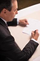 Signing a contract. Top view of mature man in formalwear signing a document photo