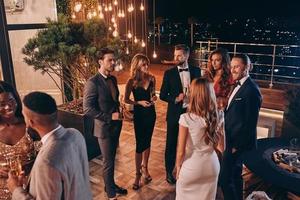 Group of people in formalwear communicating and smiling while spending time on luxury party photo