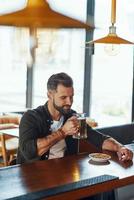 Handsome young man in casual clothing enjoying beer and smiling while spending time in the pub photo