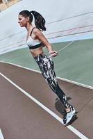 Achieving best results. Beautiful young woman in sports clothing skipping rope and smiling while exercising on the running track outdoors photo