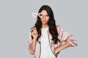 Attractive young woman wearing costume eyeglasses and looking at camera while standing against grey background photo