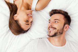 Enjoying every moment together. Top view of beautiful young loving couple lying in bed together and looking at each other photo