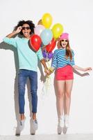 Love in all the colors of rainbows. Funky young couple holding balloons while jumping against white background photo