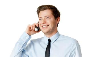 Good talk. Happy young man in shirt and tie talking on the mobile phone and looking away while standing isolated on white photo