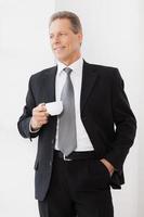 Coffee break. Cheerful senior man in formalwear holding coffee cup and smiling while standing near window photo