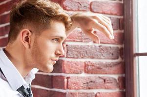 In search of new creative ideas. Handsome young man in shirt and tie holding coffee cup and looking through the window photo