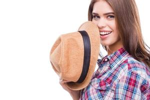 Funky beauty. Beautiful young woman in funky wear holding hat and smiling while standing against white background photo