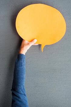 Speech bubble. Close-up of man stretching out empty speech bubble against grey background photo