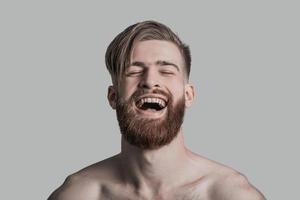 Pure happiness. Portrait of beautiful young man laughing while standing against grey background photo