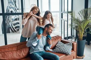 alegre familia joven sonriendo y abrazándose mientras se unen en casa foto