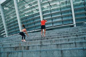 Young couple in sports clothing jumping and jogging while exercising on the steps outdoors photo