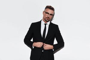 Successful businessman. Handsome young man in full suit adjusting jacket and looking at camera with smile while standing against white background photo