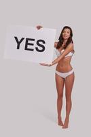 Never stop.  Full length of attractive young woman holding a poster and smiling while standing against grey background photo