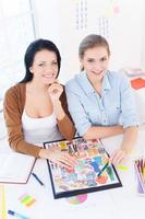 Creative executive. Top view of two young beautiful women smiling at camera while sitting at their working place photo