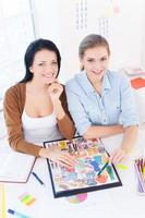 ejecutivo creativo. vista superior de dos mujeres jóvenes y hermosas sonriendo a la cámara mientras se sientan en su lugar de trabajo foto