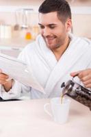 pasar la mañana del domingo en la cocina. apuesto joven leyendo el periódico y sirviendo café a la taza