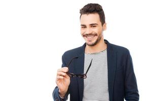 Cheerful handsome. Handsome young man holding his eyewear in hand and smiling while standing against white background photo