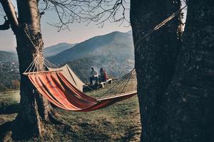 No rush. Young couple having breakfast while sitting by the campfire in mountains photo