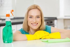 Cheerful housewife. Mature blond hair woman in yellow gloves leaning at the table and smiling photo
