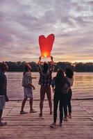 Carefree and happy. Full length of young people in casual wear preparing sky lantern while standing on the pier photo