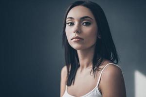 belleza pura. atractiva mujer joven mirando a la cámara con una pared gris en el fondo foto