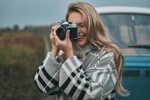 Cool shot Attractive young woman photographing and smiling while standing outdoors with the blue retro style mini van in the background photo