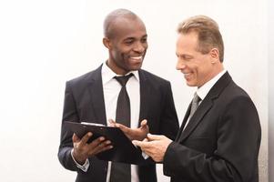 Discussing a new project. Two cheerful business men looking at the note pad and gesturing photo