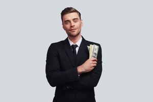 Make money now Good looking young man in full suit smiling and holding a paper currency while standing against grey background photo