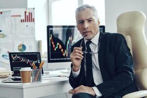 comerciante senior en negocios elegantes mirando la cámara mientras trabaja en la oficina foto