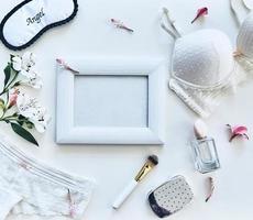 Soft sensuality. High angle shot of lingerie, sleep mask, perfume, photo frame, beauty products and flowers lying against white background