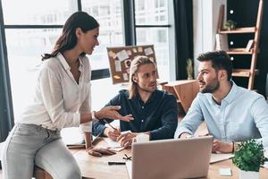 Discussing business issues. Young modern colleagues in smart casual wear working together and smiling while spending time in the office photo