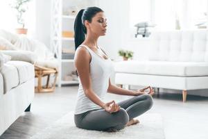 Time for yoga. Attractive young woman exercising and sitting in yoga lotus position while resting at home photo