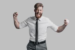 Beautiful young businessman gesturing and shouting while standing against grey background photo