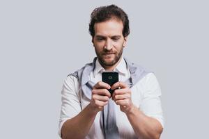 joven y exitoso. hermoso joven con ropa elegante e informal escribiendo un mensaje mientras se enfrenta a un fondo gris foto