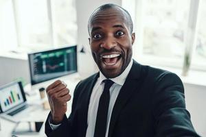 Self portrait of happy young African man in formalwear looking at camera and smiling while working in the office photo