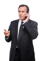 Serious business talk. Serious mature man in shirt and tie talking on the mobile phone and gesturing while standing isolated on white background photo