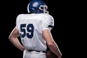 Powerful back.  Rear view of American football player holding football ball while standing against black background photo