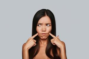 In a bad mood. Displeased young Asian woman making a face while standing against grey background photo