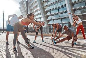 longitud total de personas con ropa deportiva calentándose y estirándose mientras hacen ejercicio en la acera al aire libre foto