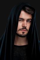 Confident and stylish. Handsome young man in hood looking at camera while standing against black background photo