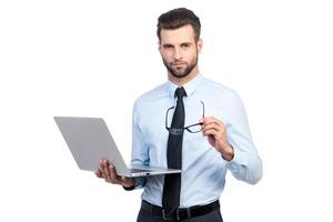 Confident business expert. Confident young handsome man in shirt and tie holding laptop and looking at camera while standing against white background photo