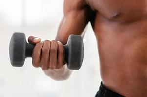 Man training with dumbbells. Cropped image of African man training with dumbbells photo